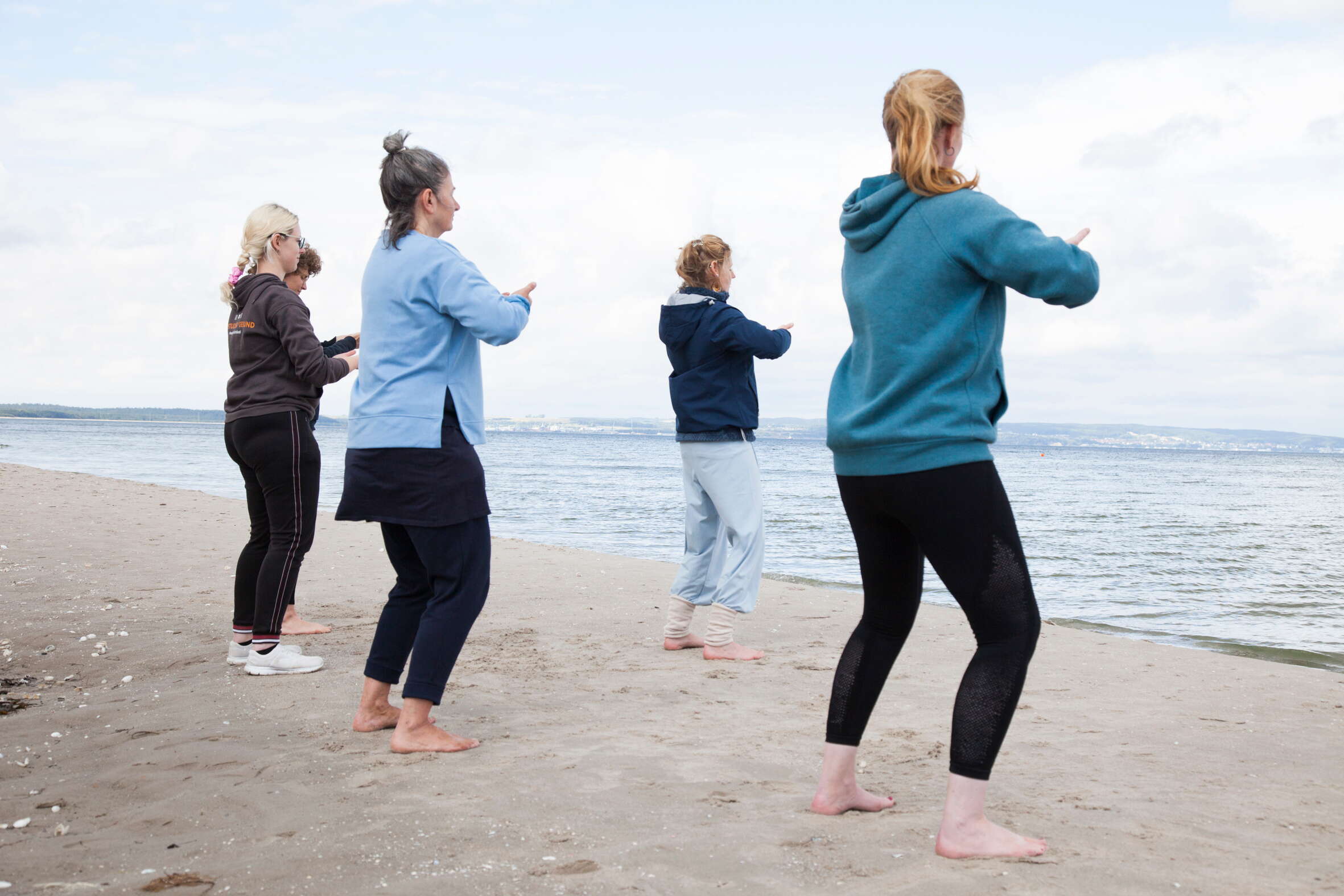 Eine Gruppe von Frauen macht Yoga am Strand, im Hintergrund das Meer